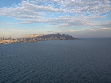 Kıyı manzarası fotoğrafçılığı, bulutlu panoramik gündüz sahili ve dağlara karşı uzak şehir