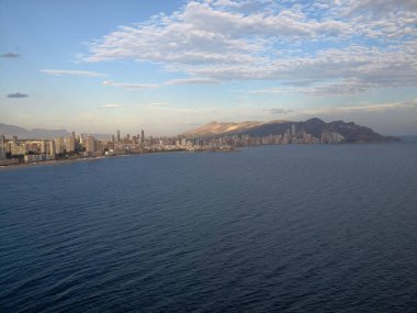 Sahil boyunca sakin bir günbatımı. Ufuk çizgisi üzerinde. Hafif okyanus dalgaları ve canlı bir gece yansıyor.