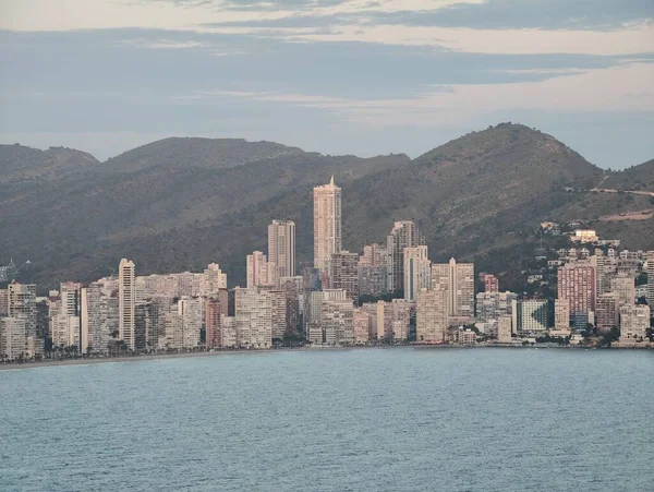 Kibar şafak, sahil kulelerini aydınlatıyor, sakin sabah, canlı şehir kıyılarında tepelerle parıldıyor.