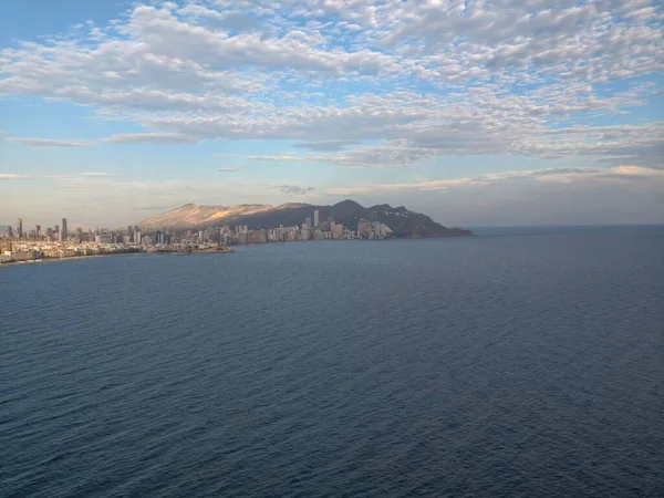 Kıyı manzarası fotoğrafçılığı, bulutlu panoramik gündüz sahili ve dağlara karşı uzak şehir
