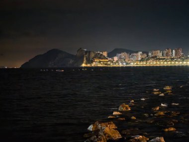 Ufuk çizgisi ve sakin sular, sakin kıyı şeridi uzak şehir ışıkları ve nazik dalgalarla aydınlandı.