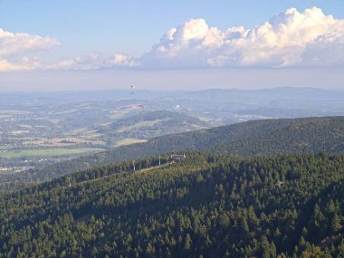 Gökyüzüne doğru orman manzarası, yemyeşil bulutlarla kaplı tepeler, yuvarlanan tepelerin üzerinde güneşli ağaçlar.