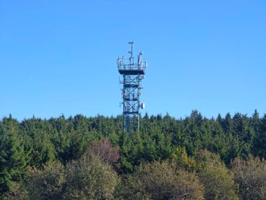 Kırsal kesimde canlı yeşillik ve açık gökyüzü içine yerleştirilmiş iletişim kulesini gösteriyor.