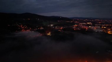 Alacakaranlıkta şehir manzarasında hafif bir sis bulutu, sisle kaplanmış sessiz mesken alanları, parlayan közle.