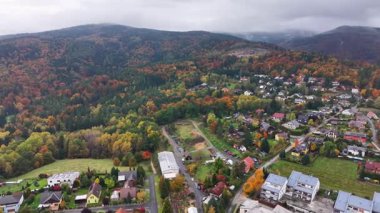 Sonbahar yeşillikleri ve sisli tepelerle çevrili yamaçlardaki topluluğu gösteren büyüleyici dron görüntüsü