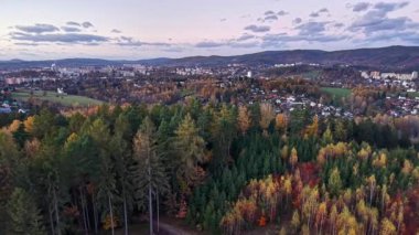 Sakin hava perspektifi parlayan ağaç tepelerini ve gün batımında uzak kasaba siluetini yakalıyor