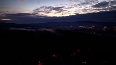 Şafak öncesi sakin manzara uzak bir aydınlanma sergiliyor. Yoğun bulutlar arasında kayboluyor.