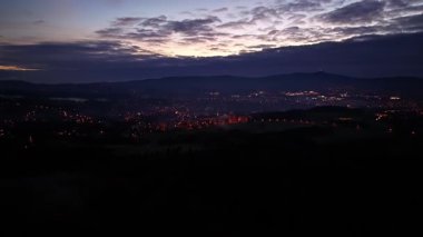 Ufuk çizgisi şafağı yuvarlanan tepeler ve bulutlarla harmanlanıyor, şehir ve tepeler üzerinde canlı gün doğumu sisli