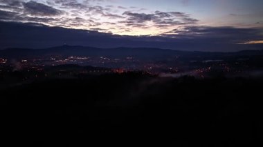 Uzak tepelerle sakin bir akşam, insansız hava aracı sakin mavi saatleri yakalıyor tepeler ve şehir ışıklarıyla