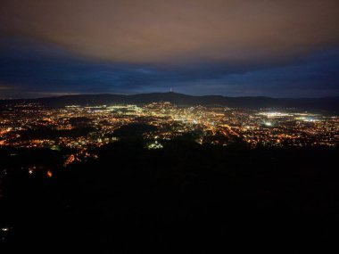 Şehir ışıkları vadi gecelerine yayıldı, alçak bulutların altında dağınık takımyıldızlar gibi parlıyordu.