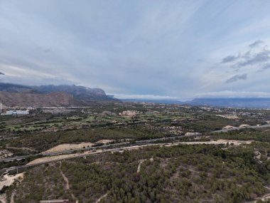Geniş vadi manzarası kara kara düşünen bulutların altında, engebeli tepeler ve soluk kıvrımlı nehir yatağı olan uzak tepeler.,