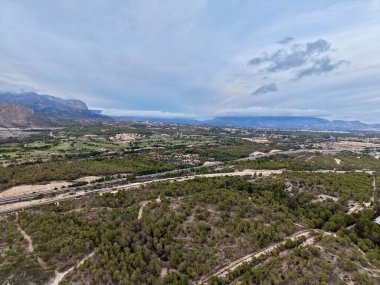 Havadan vadi manzarası, uzak dağlar, teraslı bitki örtüsü, dolambaçlı toprak yolları ve dağınık çam ağaçları.