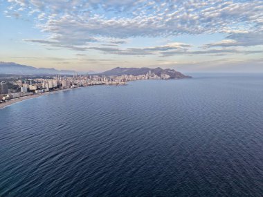 Geniş açık deniz ufku bulutların altında desenli suyu, yumuşak dalgaları ve uzak kıyı şeridini gözler önüne serer.