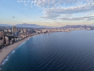 Yumuşak sabah gökyüzü altında kıyı şeridinin ve denizin havadan süpürme eğrisi, geniş bir su ve kentin kenarları.