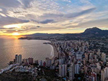 Gün batımı silueti sıcak ışıkla yükseliyor, seyahat fotoğrafçısı gökdelenlerin parıldayan yüzünü yakalıyor, sakin deniz.