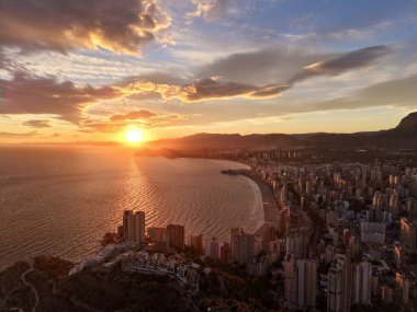 Kıyı şehrinin üzerinde gün batımı gökyüzü, gökdelenler ve körfez boyunca kıvrılan kumsallar, gökyüzü...