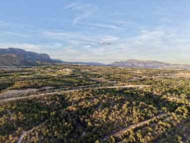 İnsansız hava aracı görünümü yuvarlanan tepeler, güneşli çalılıklar ve kıvrımlı yollar, uzun gölgeler sırtı vurguluyor ve dokulu