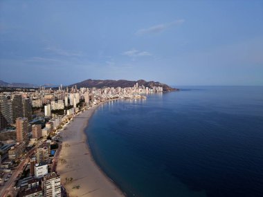 Sakin okyanus ve aydınlık gezinti güvertesi, uzun hilal plaj kıvrımları olan havadan alacakaranlık sahili ufku.