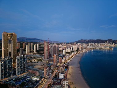 Sahile bakan lüks tavan çizgisi ve cam kuleler, parıldayan ışıklar ve teraslar yaratıyor.