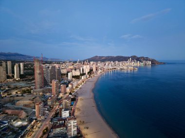 Alacakaranlık sahili ve aydınlık ufuk çizgisi. yumuşak mavi saat ışığı sakin denizi yansıtır, apartman pencereleri parlar