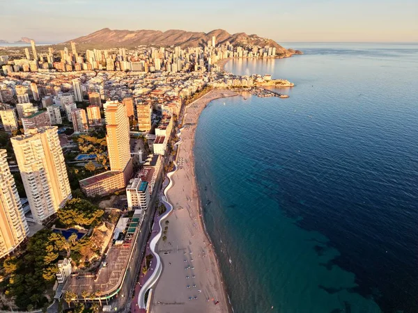 Güneşli sahil ve gökdelenli ufuk çizgisi. Altın ışık, kumu güneş banyosu ve şemsiyelerle doldurur.,