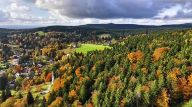 Sonbaharın kıyısında hava manzaralı köy, ormandaki renkli ağaçların arasına yuva yapmış evler, açık araziler ve dolambaçlı yollar.