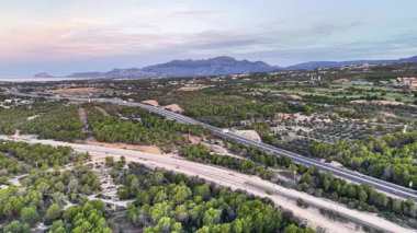 Ağaçlı ve uzak dağlı karanlık hava yolu koridoru, asfalt yolda yumuşak alacakaranlık ışığı.