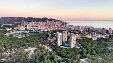 Hava Yeşilkuşağı ve Şehir Gün batımında Pastel Gökyüzü, Çam tepe örtüsü Önplanda ve Yükseklerde