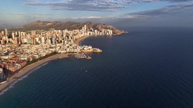 Güneşli sahil şeridinin İHA Panorama 'sı Marina ile şehir silueti, botlar ve geniş dalgalar