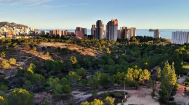 Deniz kenarına bakan güneş ışığı parkı gökdelen ve kuleler, yemyeşil ağaç örtüsü ve kıvrımlı yollar kıyı şeridi.