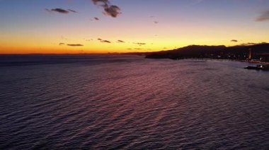 Işıl ışıl kıyı şeridi ve sakin denizi olan akşam körfezi, gezinti ışıkları parıldıyor, uzak gökyüzü ve yumuşak alacakaranlık.