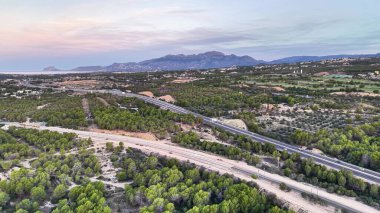 Ağaçlı ve uzak dağlı karanlık hava yolu koridoru, asfalt yolda yumuşak alacakaranlık ışığı.