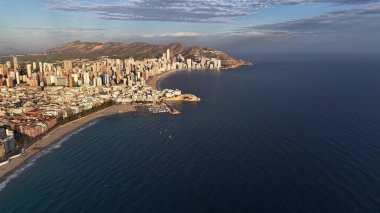 Güneşli sahil şeridinin İHA Panorama 'sı Marina ile şehir silueti, botlar ve geniş dalgalar