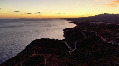 Rüzgarlı sahil yolu ve Cliffline 'ın yukarısında güneş batıyor, İHA Yörüngesi Engebeli Promontory, Uzak Dağlar' ı gözler önüne seriyor