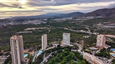 Gündoğumunda Yeşil Vadi 'ye bakan gökdelen, modern kuleler ve havuzlar, virajlı yollar, tatil köyü atmosferi.,