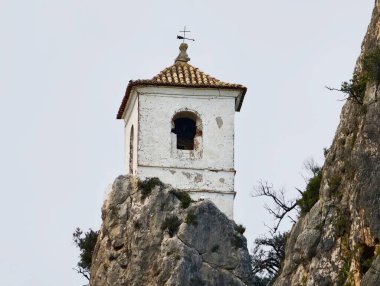 Taştan çan kulesi kayaya tünemiş, beyazlatılmış masonluk, çapraz final, yıpranmış fayanslar ve yakın çekim