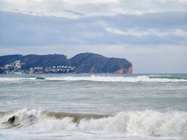 Uzak Burunlu Rüzgâr Koyu ve Rocky Shoreline üzerindeki dağınık villalar, Huzursuz Sörf Yıkama