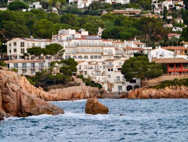 Whitewashed Villas Rocky Shoreline 'ın üzerinde tünemiş, Yoğun Yeşillik yamaçta ve Katmanlı Mimarlık