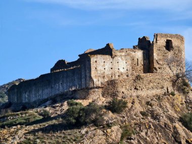 Dağılmış duvarları ve engebeli yamaçları olan, tepeden aşağıya doğru mavi gökyüzü, yosun ve ender bulunan güneşli taş kalıntıları.