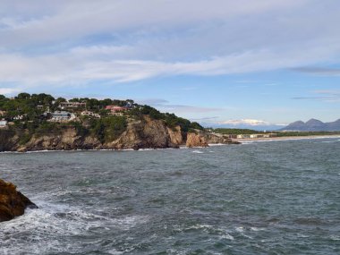 Korunaklı suları ve yapraklı burnu olan uçurum kenarındaki körfez, yumuşak dalgalar Rocky Sahili, Pastel Gökyüzü ve uzak