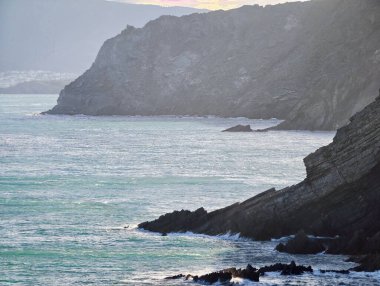Kayalıklar Sarsıntılı Turkuaz Sörf, Köpüklü Dalgalar Jagged Rock Face ve Moody Lighting 'le Çarpıştı