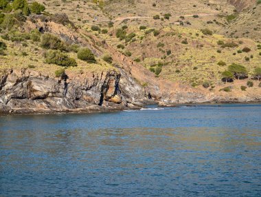 Rocky Shoreline Sakin Mavi Su Tepeleri, Açık Deniz Kucakları Güneş Işığı Altındaki Uçurumlar