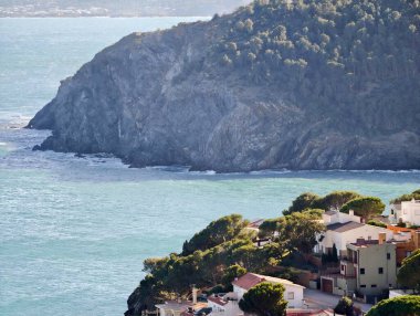 Uçurum kenarındaki evler Turkuaz Koyu 'nun üzerine tünemiş Çam Ağaçları ve Rocky Sahili, Aydınlatıcı Teras Işığı