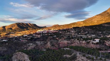 Dusk Ridge aşağıdaki küçük kasabayı çerçeveliyor, Gölgeli Orman ve Rocky ön planda, Pastel Gökyüzü Stratus ile