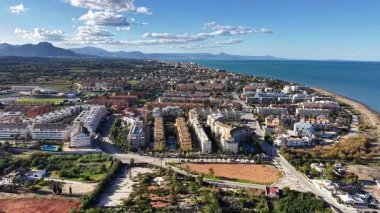 Deniz kenarındaki caddeleri, desenli çatıları ve yeşil parkı, gök mavisi deniz kıvrımları olan güneşli sahil banliyöleri