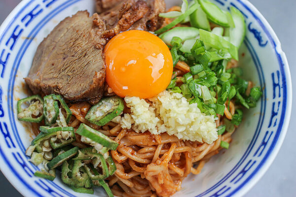 Thai-Sichuan style Red Pork Noodles (Ramen) with char siu, a raw egg yolk, and unique vegetable additions like okra. This rich and savory Thai street food is a delicious Asian fusion.