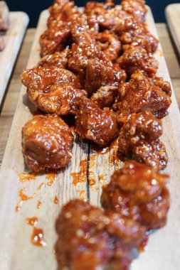 Kavrulmuş Kore usulü kızarmış tavuk Dakgangjeong tatlı ve baharatlı kırmızı sosla kaplanmış, kırsal ahşap bir tahtanın üzerinde servis ediliyor. Parlak dokusuyla klasik Asya konforlu yemekleri..