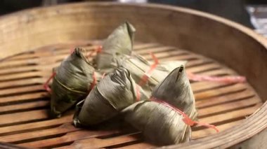Geleneksel ahşap bir sepetin içinde buharlaşan Zongzi 'nin (Çin Yapışkan Pirinç Böreği) yakın çekim videosu. Sıcak buhar yükseliyor, şenlikli, otantik Asya yemek pişirme sürecini vurguluyor.