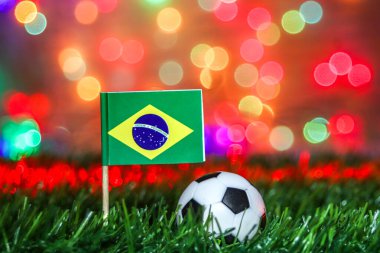Brezilya bayrağının canlı bir tasviri ve stadyum ışıkları ve renkli bokeh ile vurgulanmış çimlerin üzerinde bir futbol topu. Spor promosyonları için ticari açıdan güçlü, şampiyon ruhunu taşıyor..