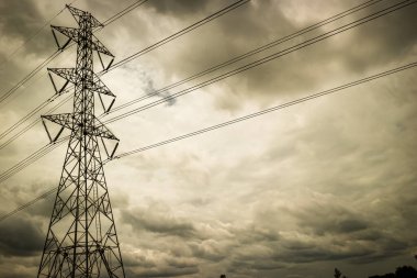 Yüksek voltaj iletim kulesinin, bulutlu bir tropikal gökyüzüne karşı yükselen, enerji krizini, altyapı gücünü ve endüstriyel gerilimi sembolize eden sepia tonlu dramatik bir sahnesi..